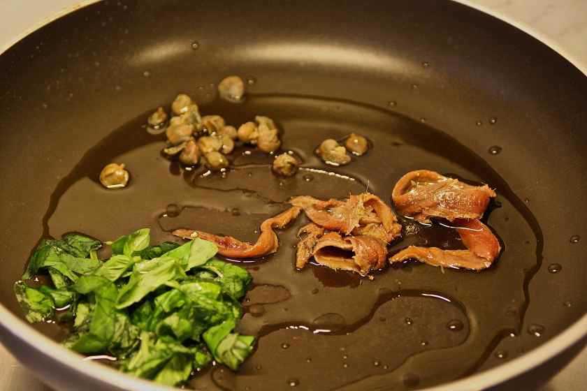 riporre in una padella antiaderente: capperi, basilico ed alici sott'olio