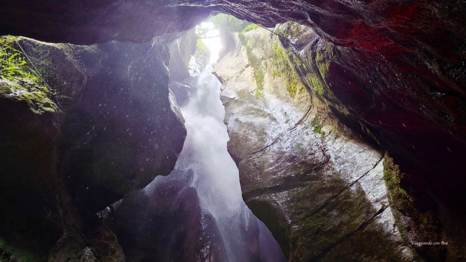 Una vista dall'interno di una gola con una cascata che scorre tra le rocce, illuminata dalla luce naturale che entra dall'alto.