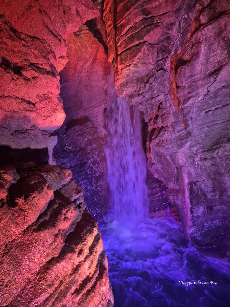 Una cascata che scorre tra pareti rocciose illuminate da luci colorate.